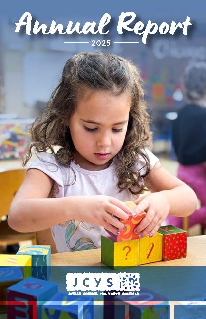 A young girl sits at a table, stacking colorful blocks. The image is the cover of a 2025 annual report for JCYS, with the title and organization logo displayed at the top and bottom of the page.