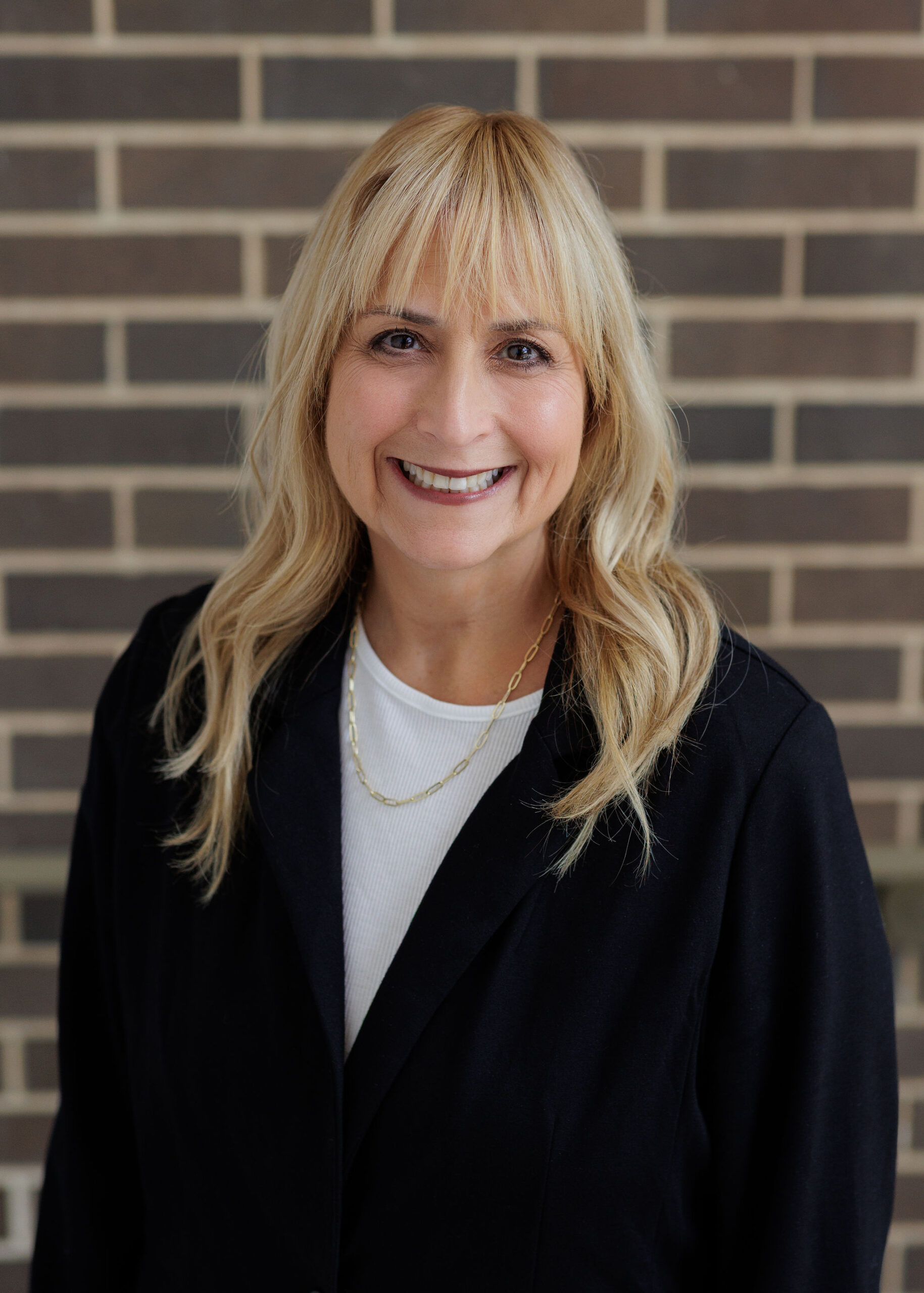 A woman with blonde hair smiling while wearing a black blazer over a white shirt.