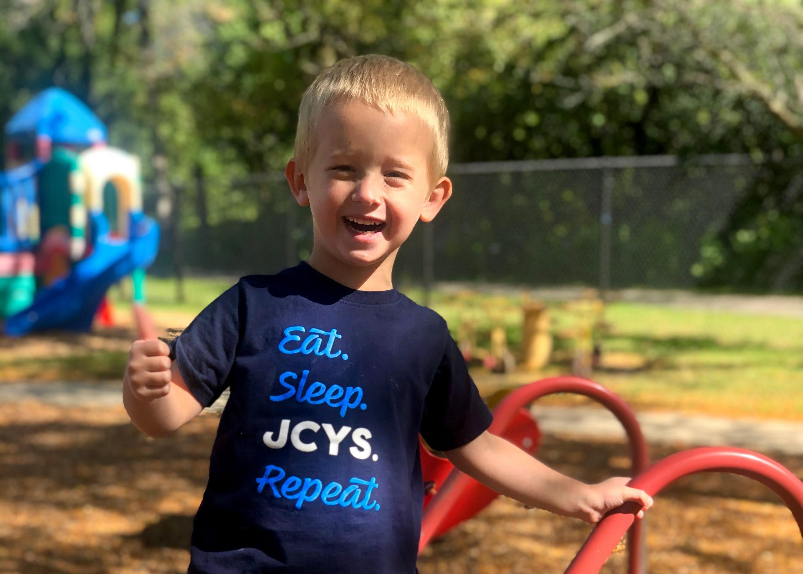 Boy outside giving thumbs up and wearing Eat. Sleep. JCYS. Repeat. shirt