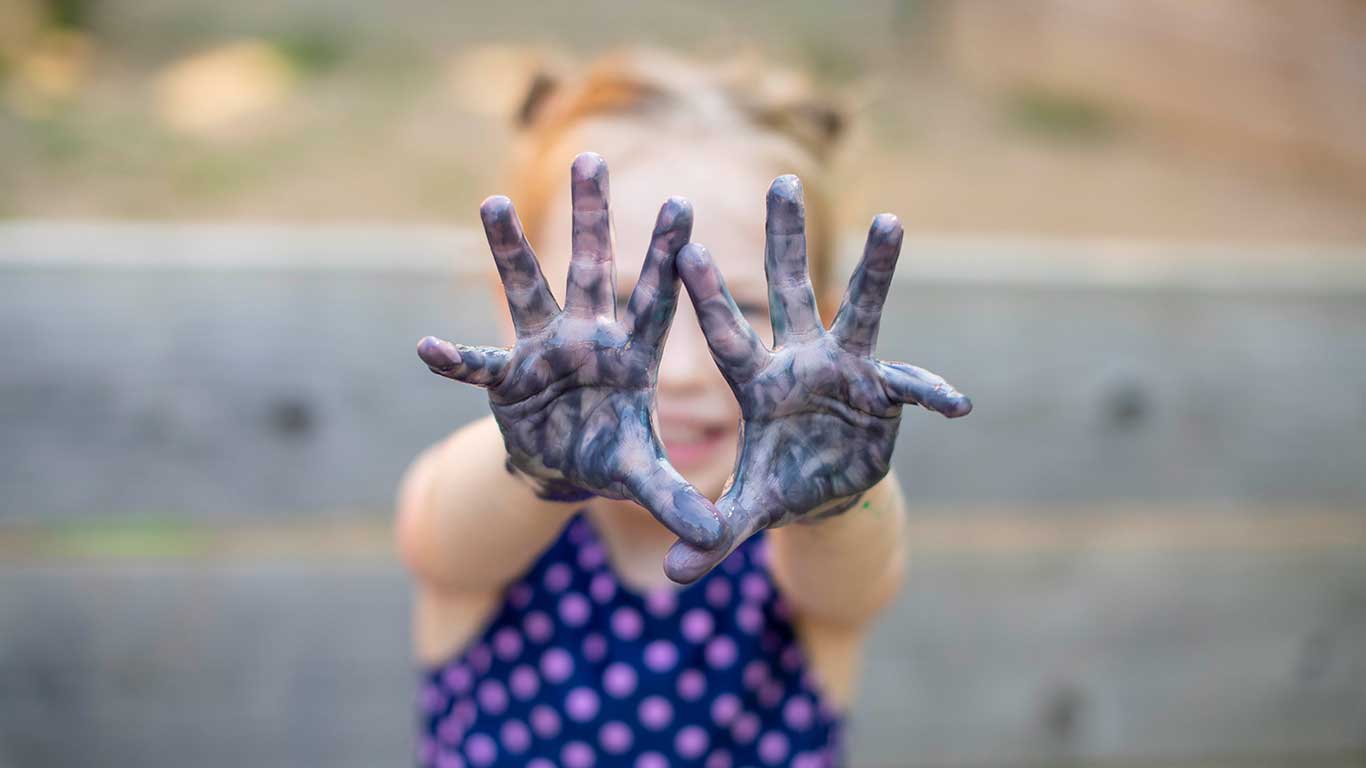 Child with painted hands. They are holding their hands in front of their face and showing their palms. Links to toddler and preschool page.