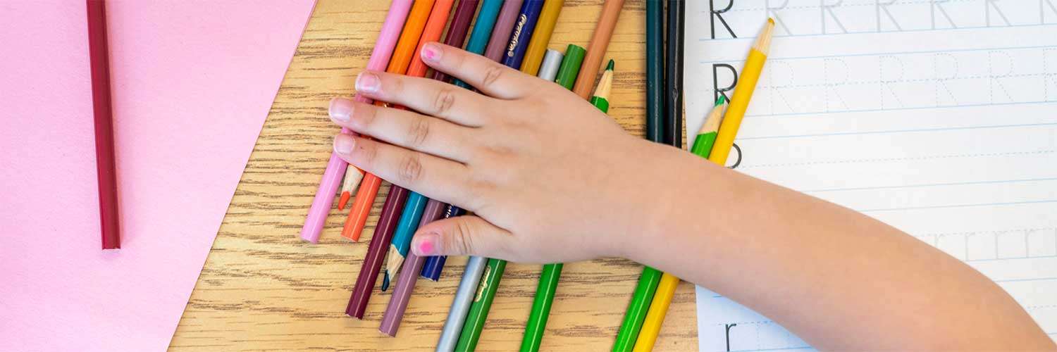 Colored pencils on a table with a hand