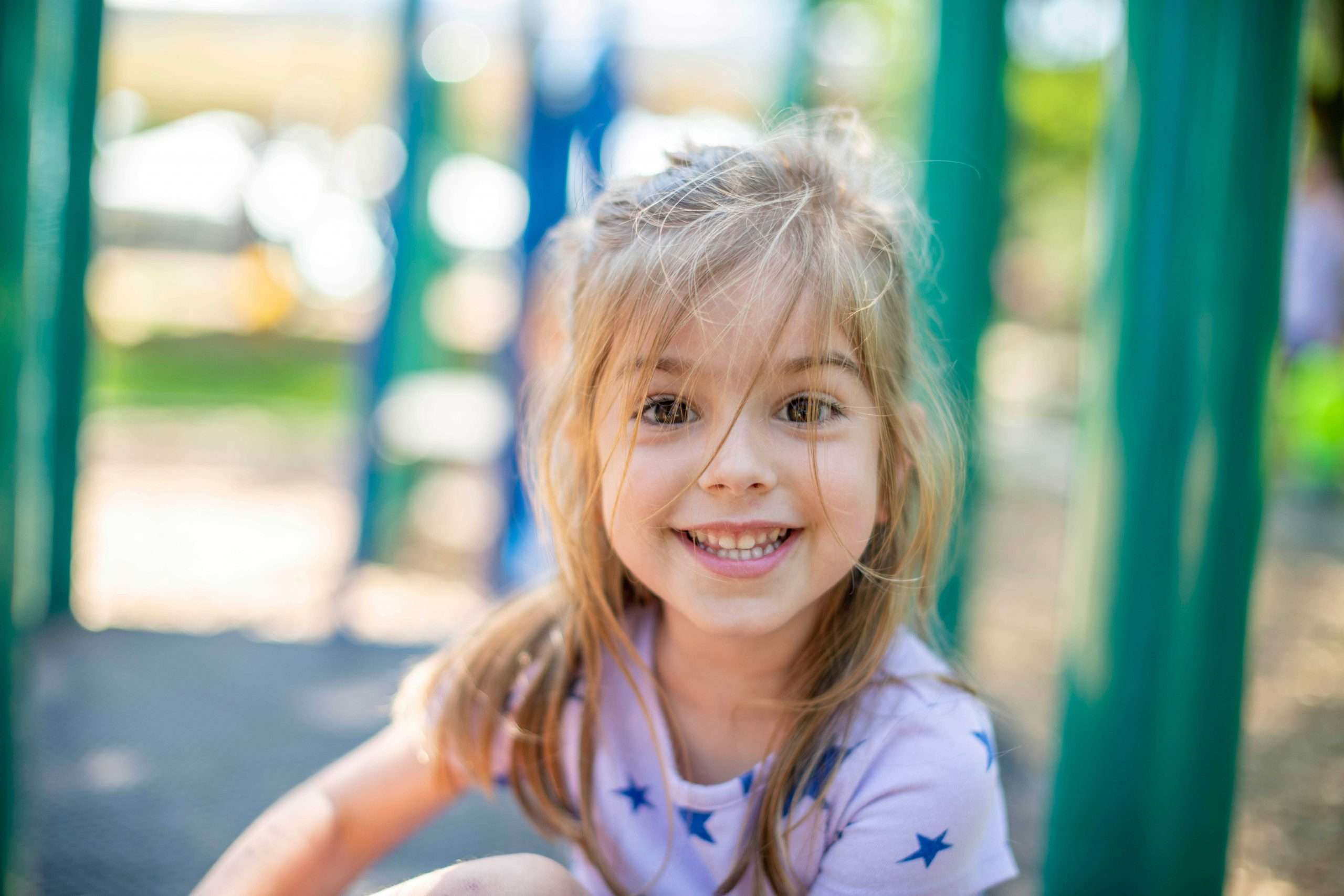 Girl with bangs looking directly at the camera and smiling. She is sitting on playground equipment at JCYS Northwest Family Center.