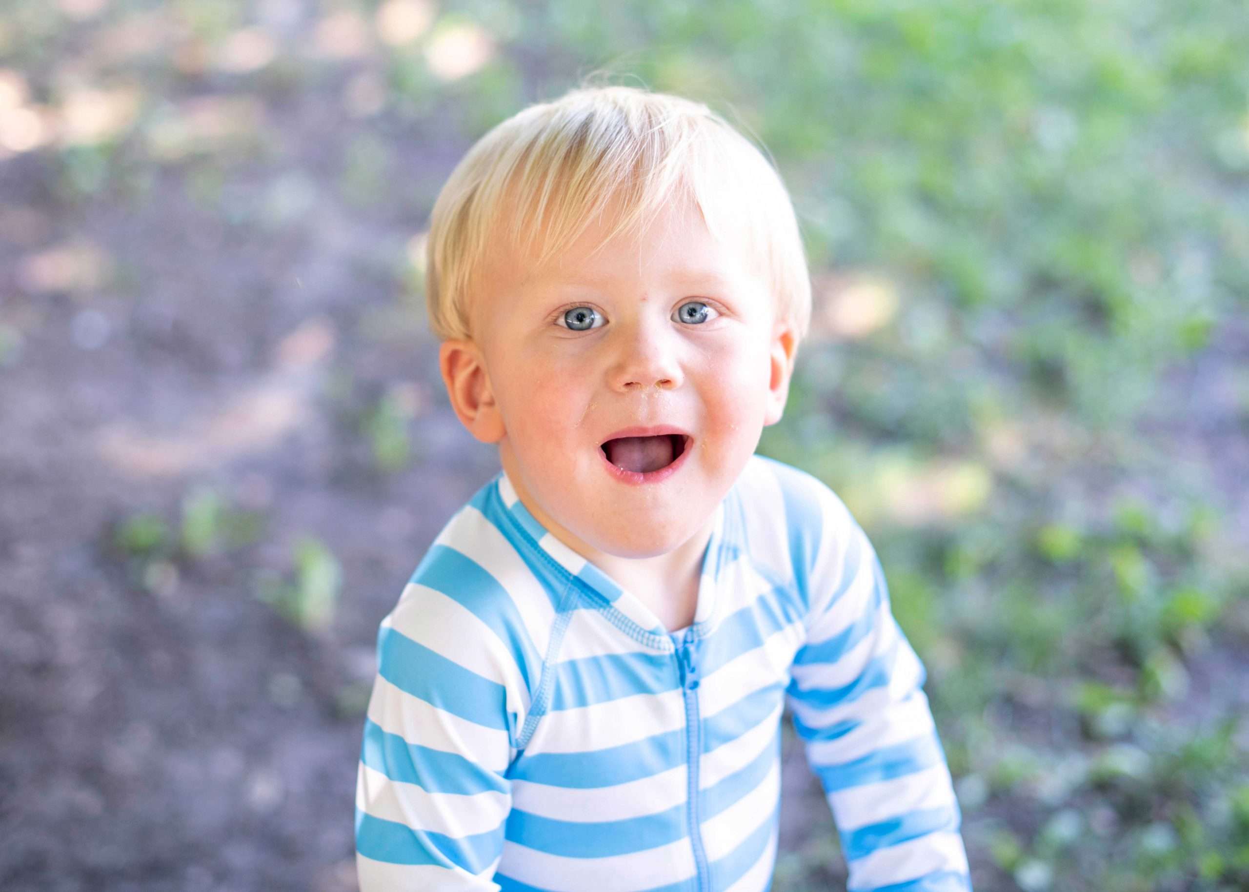 Smiling toddler looking up at the camera. They're wearing a striped blue onesie.