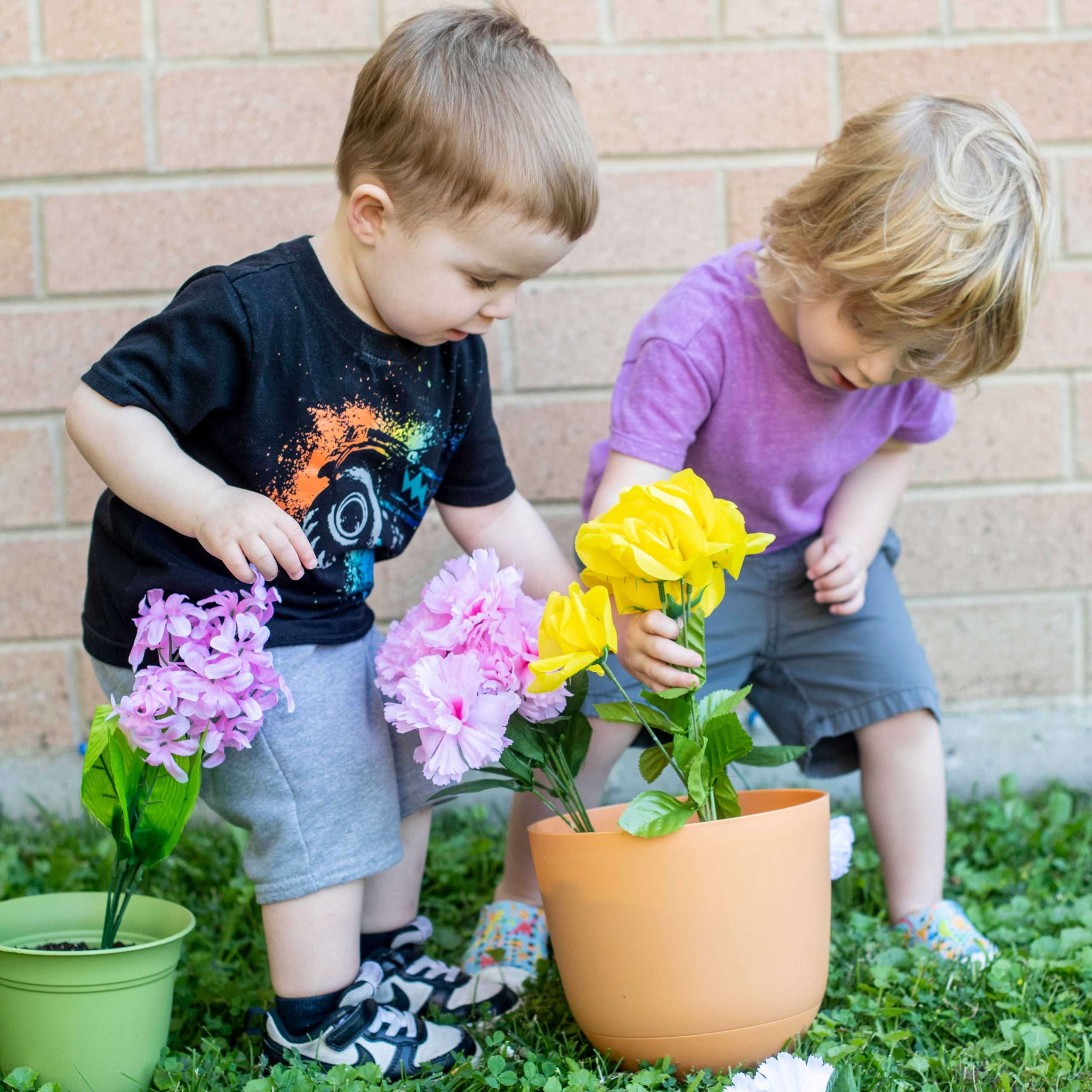 Two toddlers "planting" flowers in dirt outside of Northwest Family Center